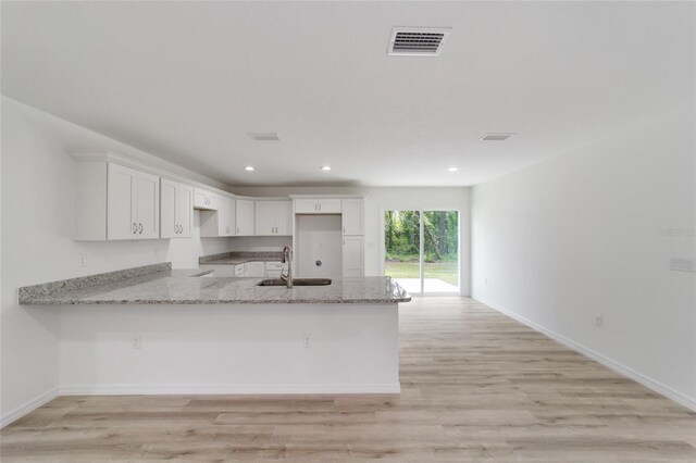 kitchen featuring white cabinetry, kitchen peninsula, light hardwood / wood-style flooring, and light stone countertops