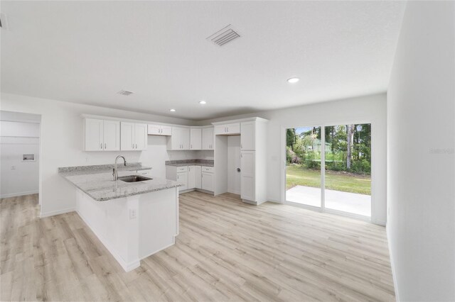 kitchen with sink, kitchen peninsula, light hardwood / wood-style floors, and white cabinetry