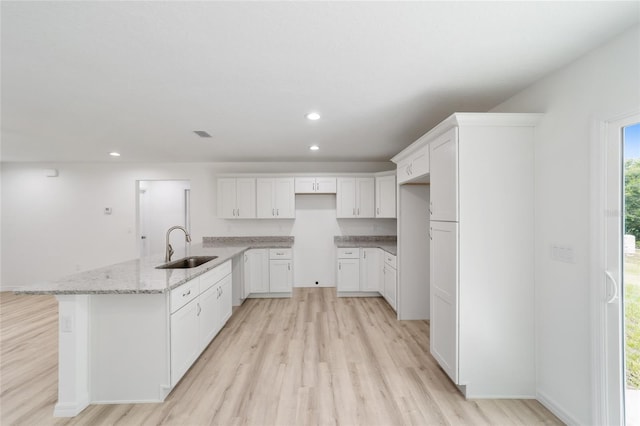 kitchen with white cabinetry, sink, light stone counters, light hardwood / wood-style flooring, and kitchen peninsula