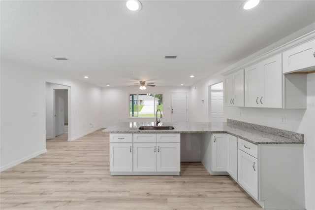 kitchen with ceiling fan, white cabinets, light wood-type flooring, sink, and kitchen peninsula