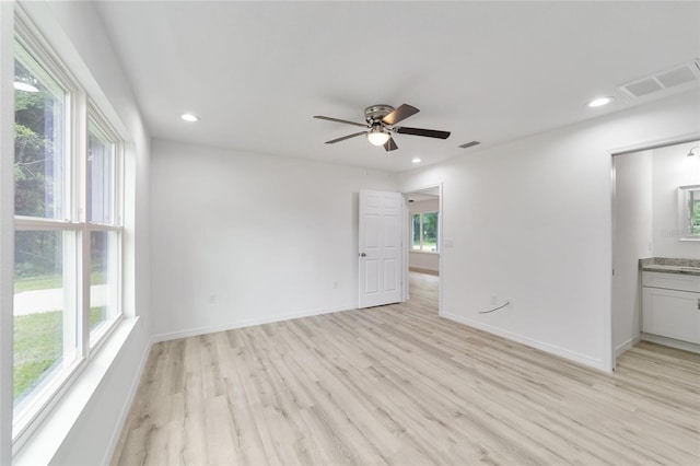 interior space with ensuite bathroom, multiple windows, ceiling fan, and light wood-type flooring