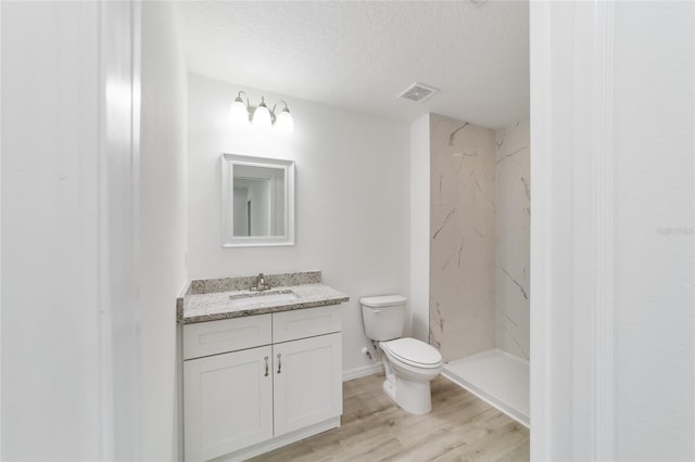 bathroom featuring vanity, hardwood / wood-style flooring, a tile shower, toilet, and a textured ceiling