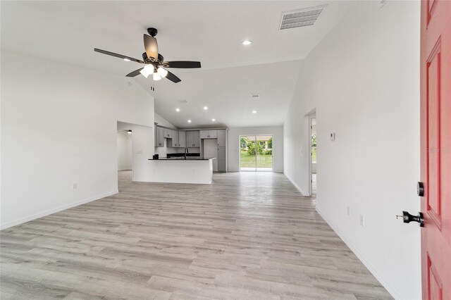 unfurnished living room with sink, high vaulted ceiling, ceiling fan, and light wood-type flooring