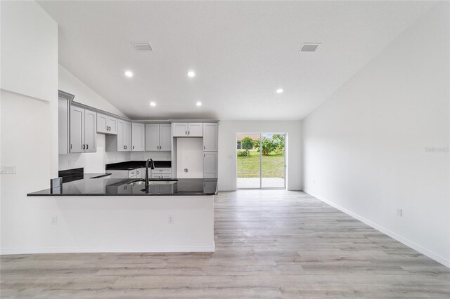 kitchen featuring light hardwood / wood-style flooring, lofted ceiling, kitchen peninsula, and gray cabinetry