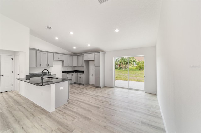 kitchen with gray cabinetry, kitchen peninsula, light hardwood / wood-style floors, sink, and high vaulted ceiling