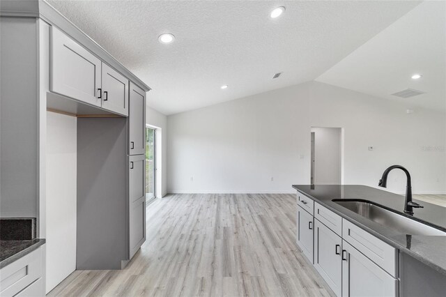 kitchen with light hardwood / wood-style flooring, vaulted ceiling, sink, gray cabinets, and a textured ceiling