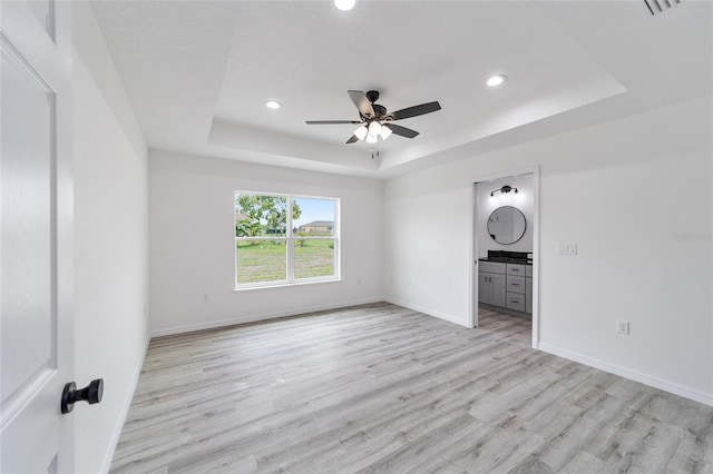 unfurnished living room featuring ceiling fan, a raised ceiling, and light hardwood / wood-style floors