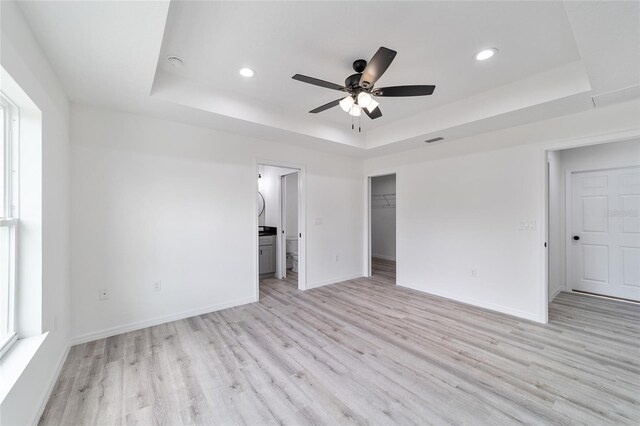 empty room with ceiling fan, light wood-type flooring, a tray ceiling, and a healthy amount of sunlight