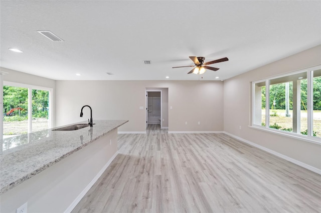 unfurnished living room featuring light hardwood / wood-style floors, a wealth of natural light, sink, and ceiling fan