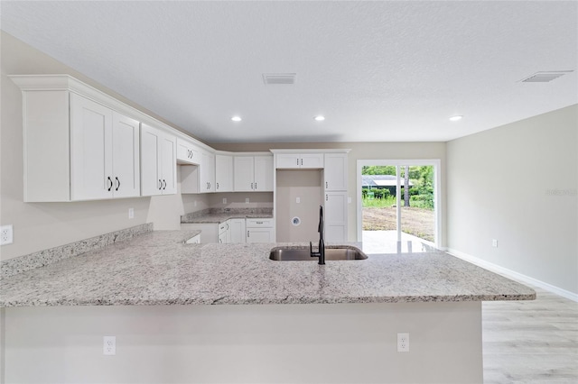 kitchen featuring sink, light stone countertops, white cabinets, and light hardwood / wood-style floors