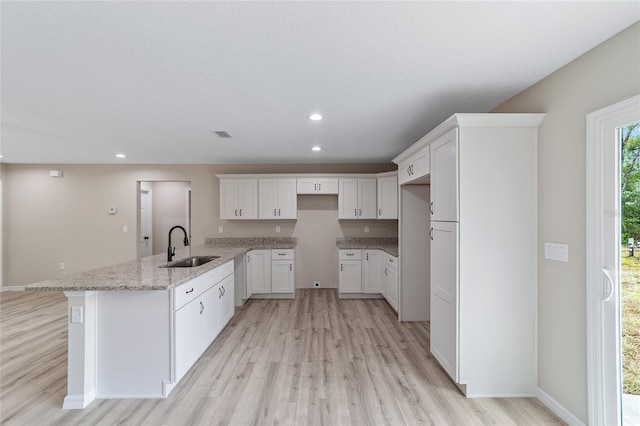 kitchen featuring white cabinets, sink, light stone counters, kitchen peninsula, and light wood-type flooring