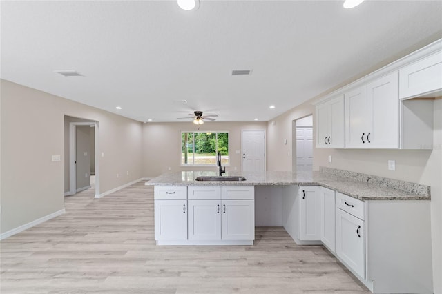 kitchen with white cabinets, light stone counters, ceiling fan, light hardwood / wood-style floors, and sink