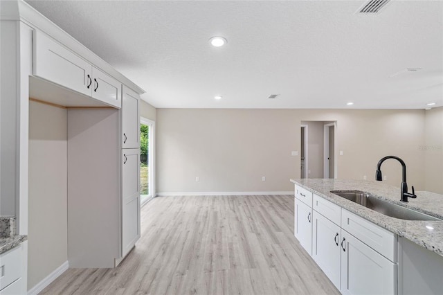 kitchen with sink, white cabinets, light stone counters, and light wood-type flooring