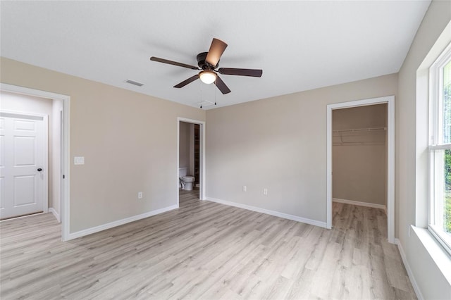 unfurnished bedroom with a spacious closet, ensuite bathroom, a closet, light hardwood / wood-style floors, and ceiling fan