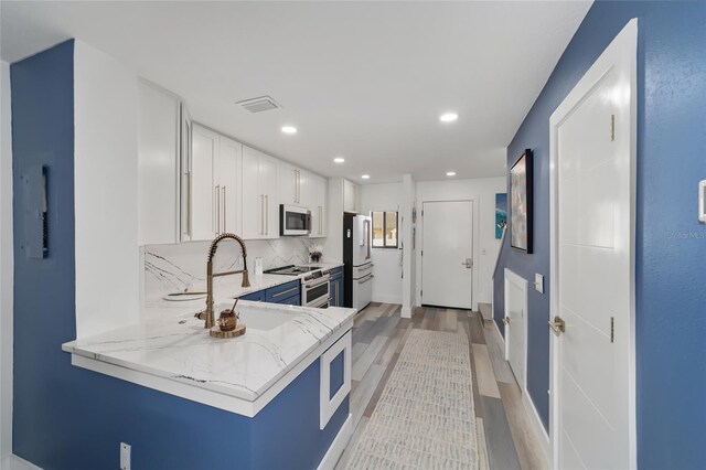 kitchen with premium appliances, white cabinetry, backsplash, light hardwood / wood-style floors, and sink