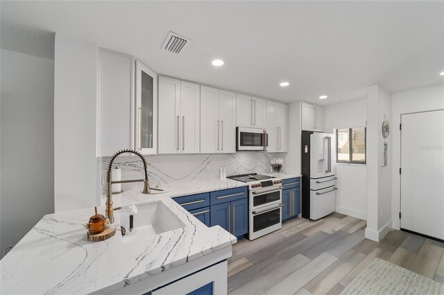 kitchen with light hardwood / wood-style floors, blue cabinetry, light stone countertops, and high end appliances