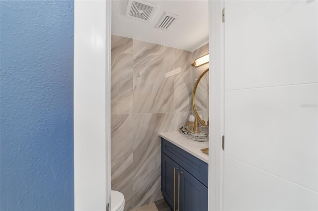 bathroom with vanity, toilet, and tile walls