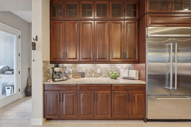 kitchen with light stone countertops, stainless steel built in fridge, backsplash, and light tile patterned flooring