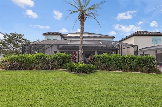 rear view of house with glass enclosure and a lawn