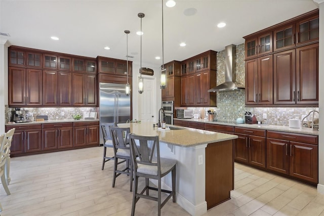 kitchen featuring a center island with sink, stainless steel appliances, wall chimney range hood, and tasteful backsplash