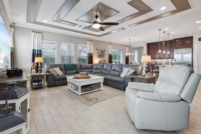 living room with ceiling fan with notable chandelier, a raised ceiling, crown molding, and light hardwood / wood-style floors