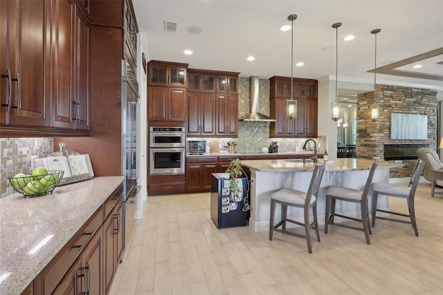 kitchen with a breakfast bar area, light hardwood / wood-style flooring, a kitchen island with sink, decorative backsplash, and wall chimney range hood