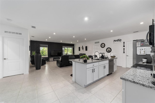 kitchen featuring a kitchen island with sink, appliances with stainless steel finishes, light stone countertops, sink, and white cabinetry