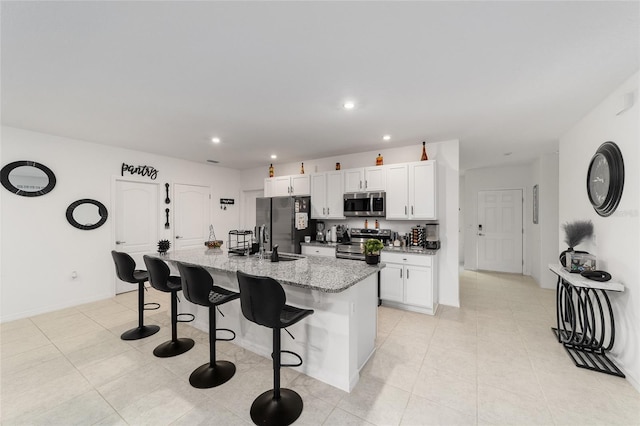 kitchen with white cabinetry, appliances with stainless steel finishes, light stone countertops, light tile patterned flooring, and a center island with sink