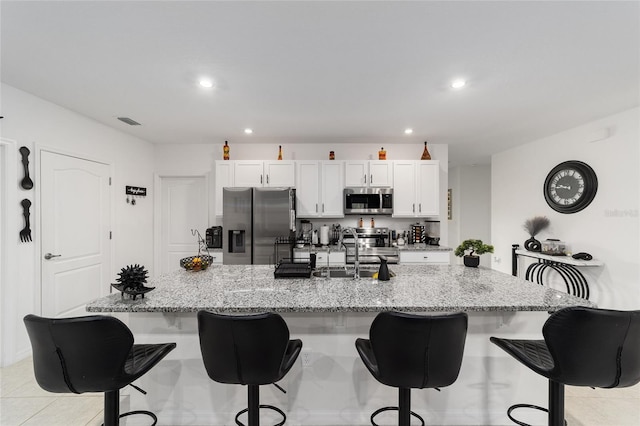 kitchen with appliances with stainless steel finishes, light tile patterned flooring, white cabinets, and a kitchen bar