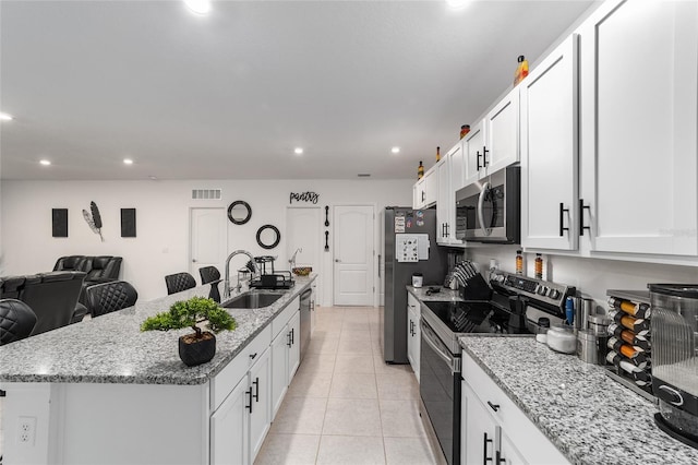 kitchen featuring light tile patterned flooring, stainless steel appliances, a kitchen island with sink, white cabinets, and sink