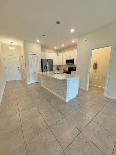 kitchen featuring appliances with stainless steel finishes, a kitchen island with sink, hanging light fixtures, white cabinets, and light tile patterned flooring