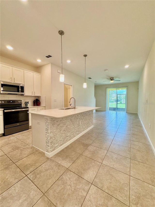 kitchen with sink, electric range, an island with sink, pendant lighting, and white cabinets