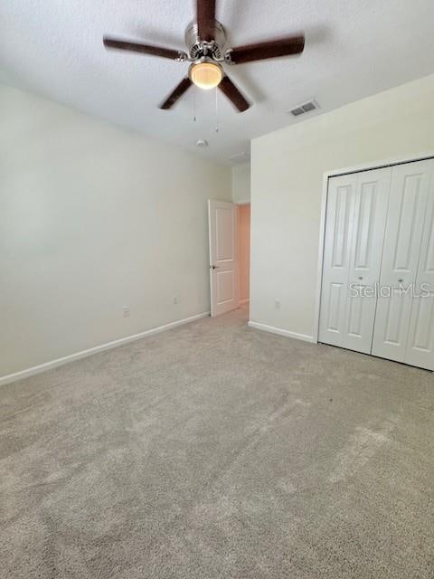 unfurnished bedroom with ceiling fan, light colored carpet, a textured ceiling, and a closet