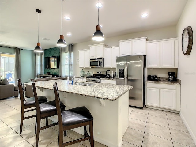 kitchen with light stone counters, an island with sink, pendant lighting, stainless steel appliances, and white cabinets