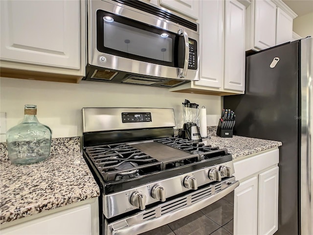 kitchen with white cabinetry, appliances with stainless steel finishes, tile patterned flooring, and light stone counters