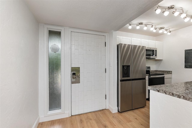 kitchen with light wood-style flooring, appliances with stainless steel finishes, white cabinetry, a textured ceiling, and baseboards