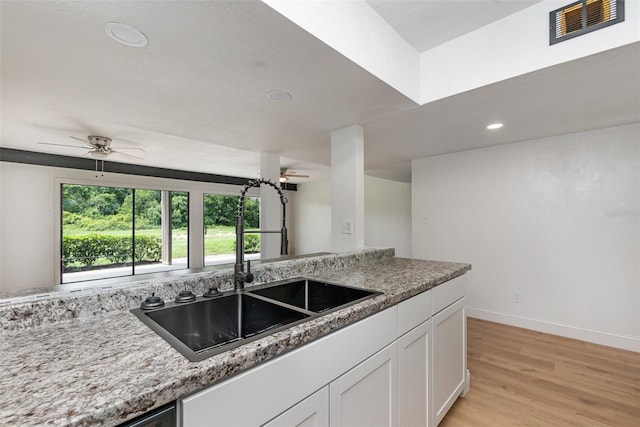 kitchen featuring light wood-style flooring, a sink, visible vents, white cabinetry, and light stone countertops