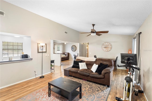 living room featuring light wood-type flooring, ceiling fan, a wealth of natural light, and a textured ceiling