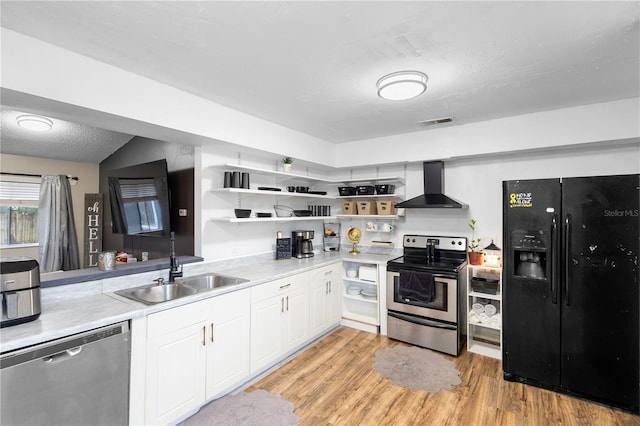 kitchen with wall chimney range hood, sink, white cabinetry, light wood-type flooring, and stainless steel appliances