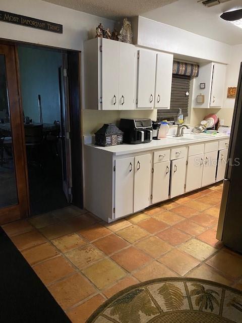 709 N Disston, Tavares, FL 32778 - kitchen with light countertops, freestanding refrigerator, white cabinets, a sink, and stone tile floors