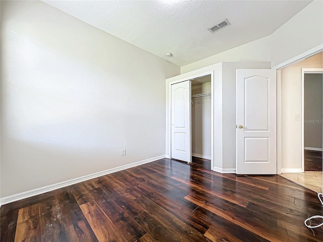 unfurnished bedroom with a textured ceiling, dark hardwood / wood-style floors, and a closet