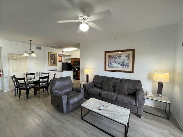 living area with light wood finished floors, baseboards, visible vents, and ceiling fan with notable chandelier