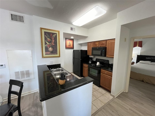 kitchen featuring visible vents, dark countertops, brown cabinets, black appliances, and a sink