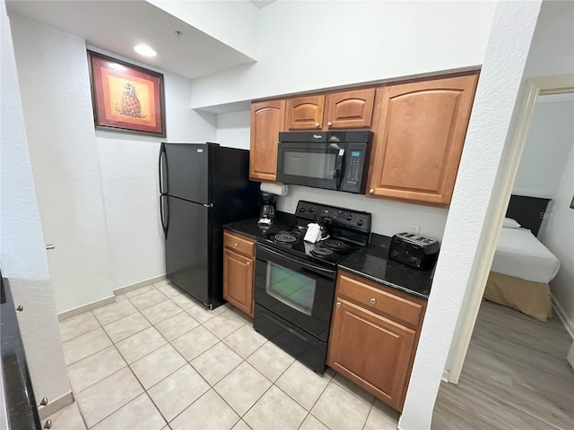 kitchen with black appliances, baseboards, dark stone counters, and brown cabinets