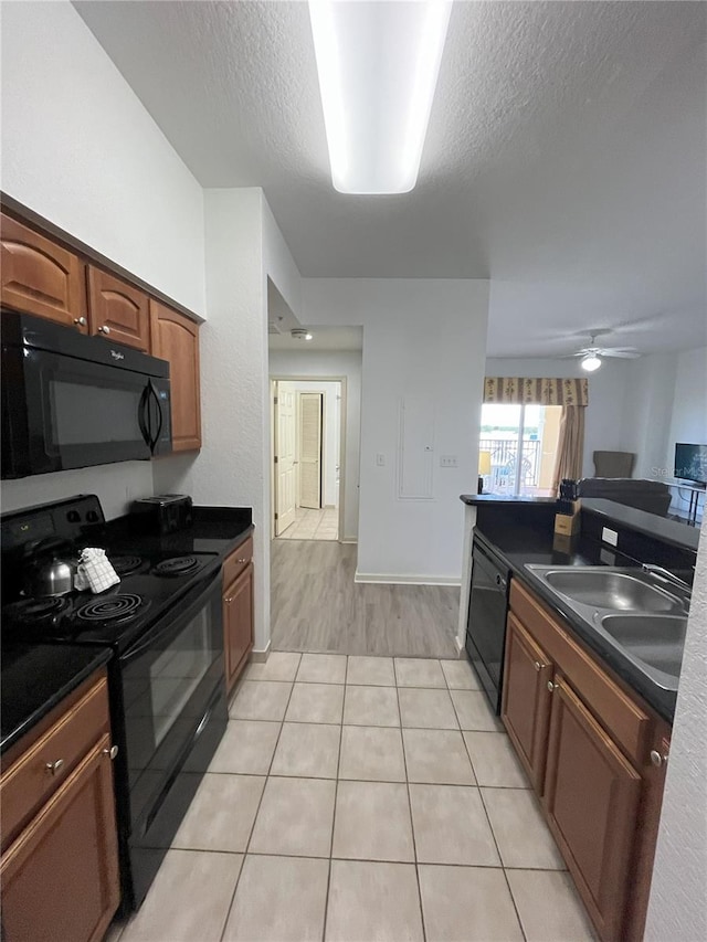 kitchen with dark countertops, brown cabinetry, a sink, a textured ceiling, and black appliances