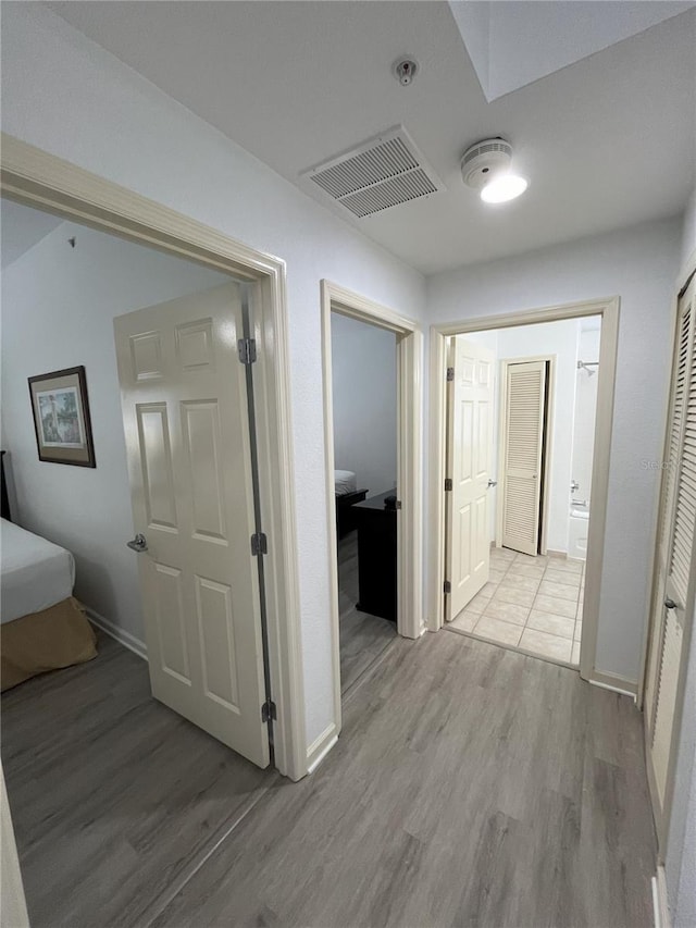 corridor with light wood-type flooring, baseboards, and visible vents