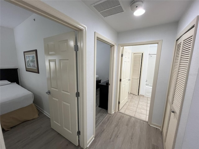 corridor featuring light wood-type flooring, visible vents, and baseboards