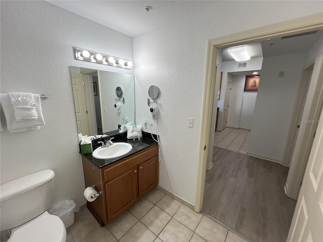 bathroom with a textured wall, toilet, visible vents, vanity, and tile patterned floors