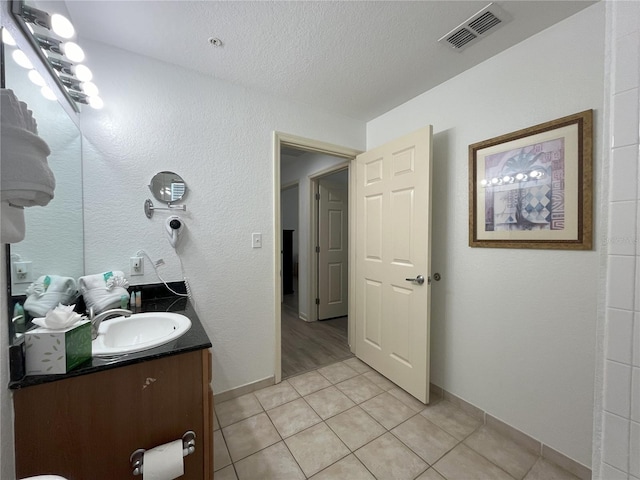 bathroom featuring visible vents, a textured wall, vanity, a textured ceiling, and tile patterned flooring