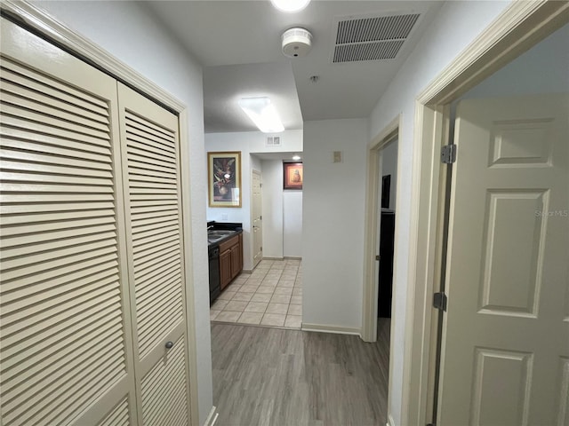 hall featuring baseboards, a sink, visible vents, and light wood-style floors